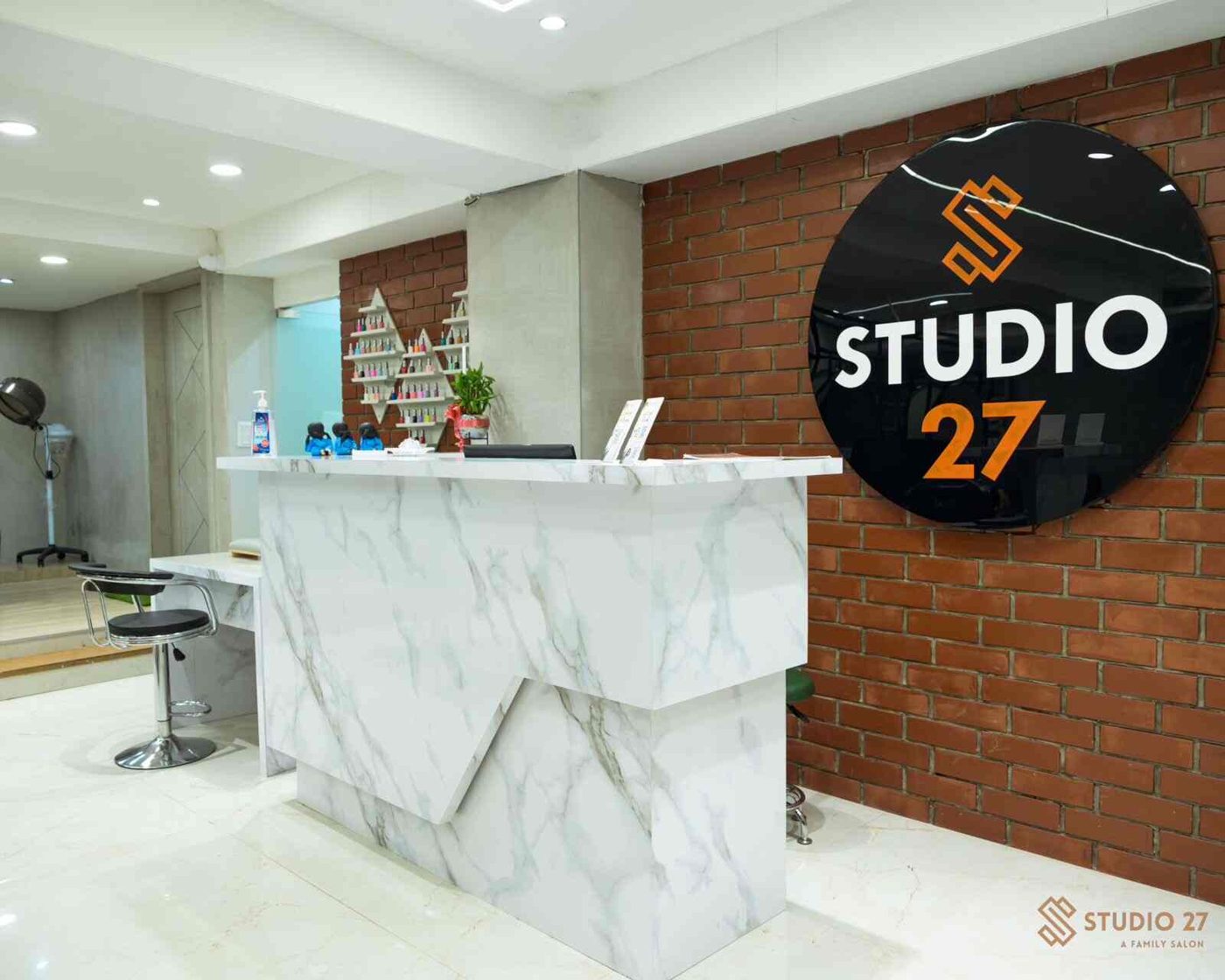 Studio 27 reception: white marble desk, brick wall and the round Studio 27 sign